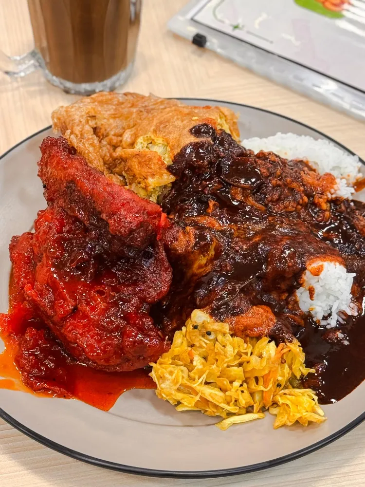 A Yaseem nasi kandar plate with a fried omelette on top, red chilli chicken, turmeric cabbage and rice under dark kuah